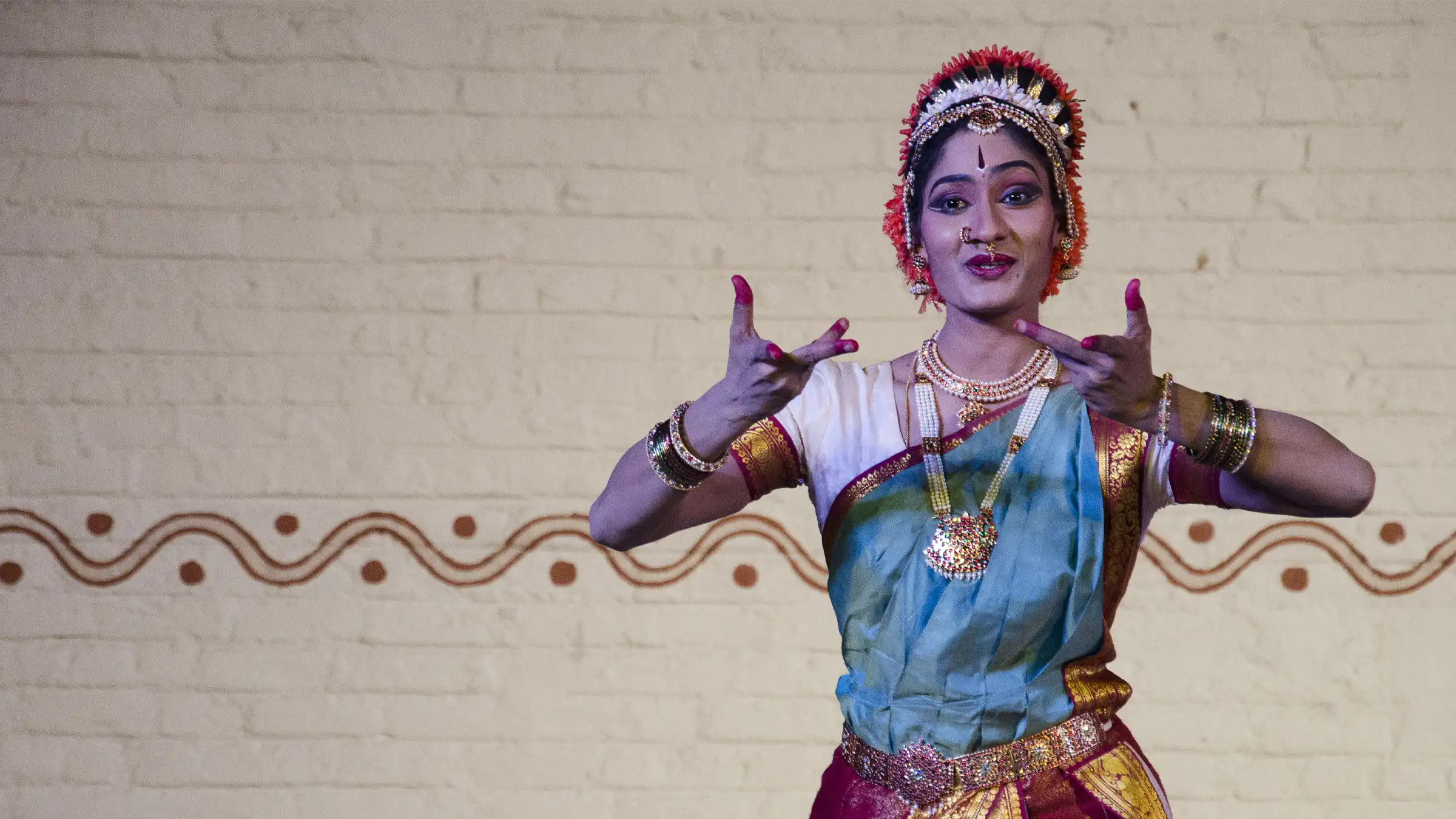 Dr. Srijayanthi in Kuchipudi costume, hands in a mudra, before a painted wall